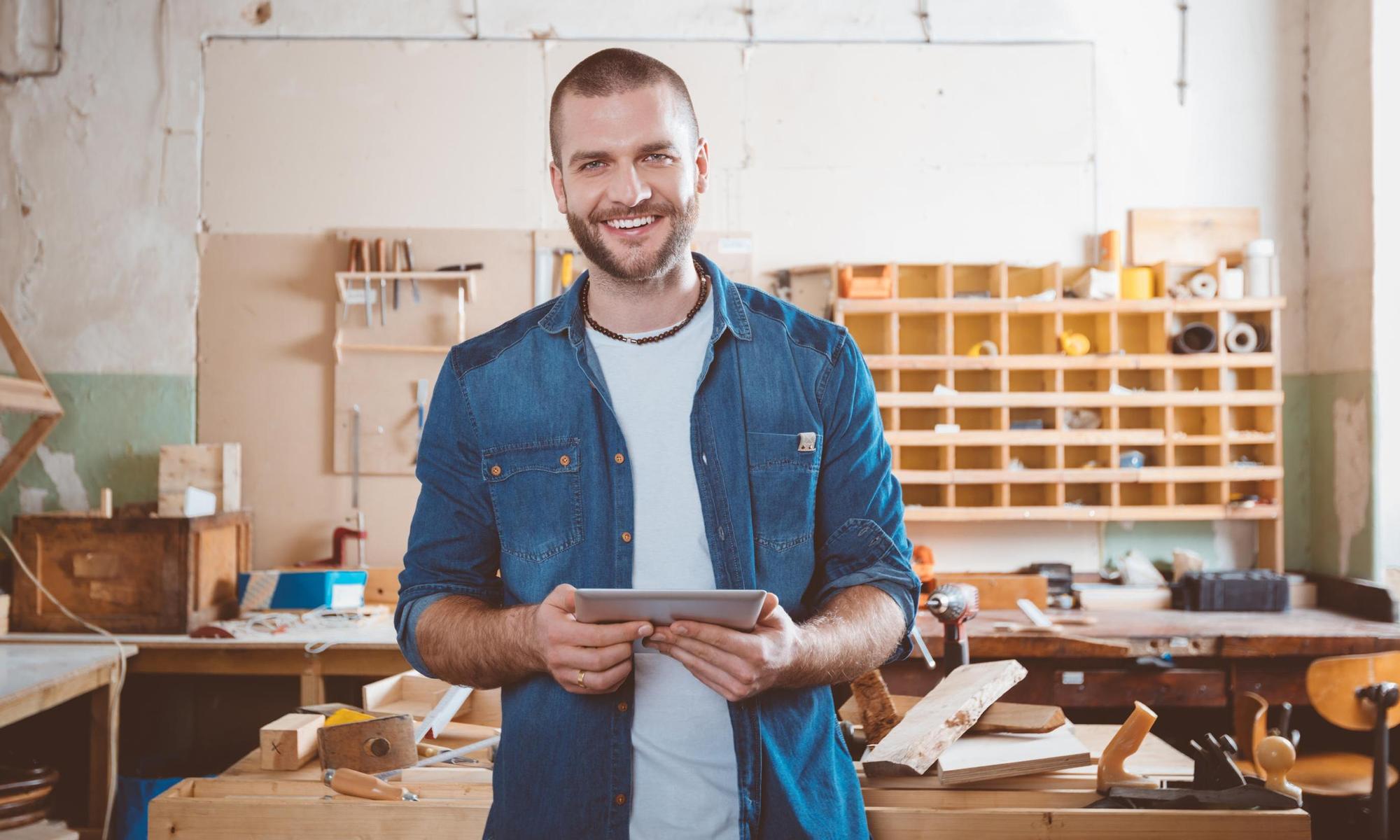 Young man in a carpentry workshop, holding a digital tablet in hands