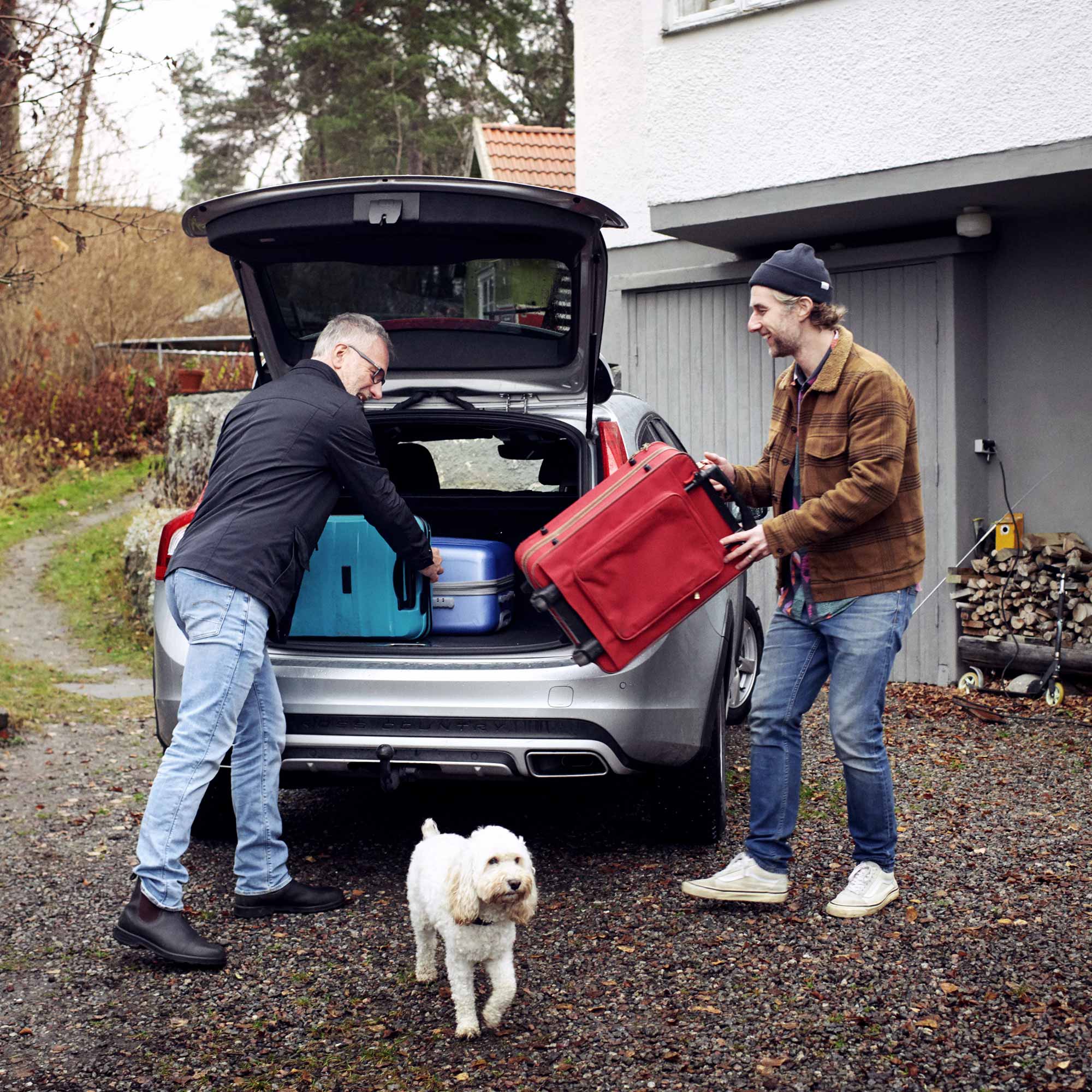 Två män packar in resväskor i bagageluckan på en bil